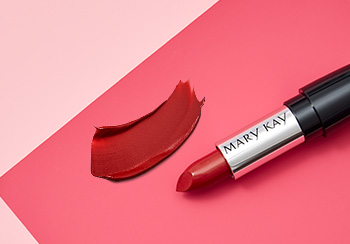 Červený rúž Mary Kay vyfotografovaný s uzáverom položeným na ružovom pozadí vedľa ukážky farby na pery.