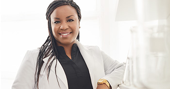 Fotografia Dr. Shoná Burkes-Hendersonovej, vedeckej pracovníčky klinického výskumu, vedkyne s tmavou pleťou, usmieva sa, prostredie navodzuje atmosféru vedeckého výskumu