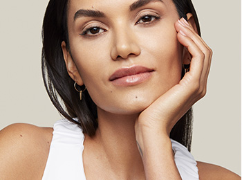 Žena s hnedými vlasmi s hydratovanou pleťou na belavom pozadí. 