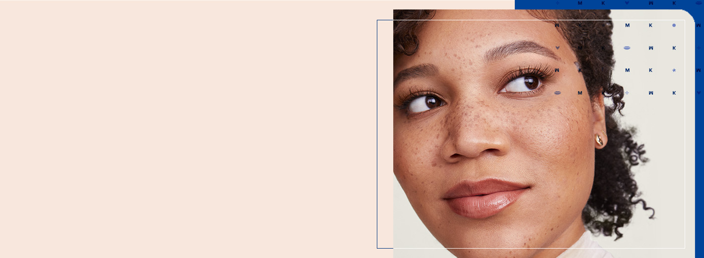 Mladá žena s pehami a sčesanými brčkavými vlasy sa usmieva a pozerá sa do strany na svetlo a tmavo modrom štruktúrovanom pozadí.