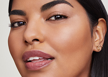 Mladá žena s hnedými rovnými vlasy pozerajúca sa priamo do kamery; usmieva sa s pootvorenými ústami, jej oči sú rozžiarené.