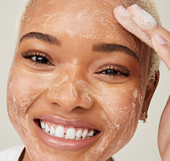 Usmievavá žena afrického pôvodu robí peeling s prípravkom Botanical Effects Povzbudzujúci peeling.